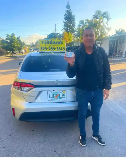 Student Liam holding his license next to a William’s Driving School car