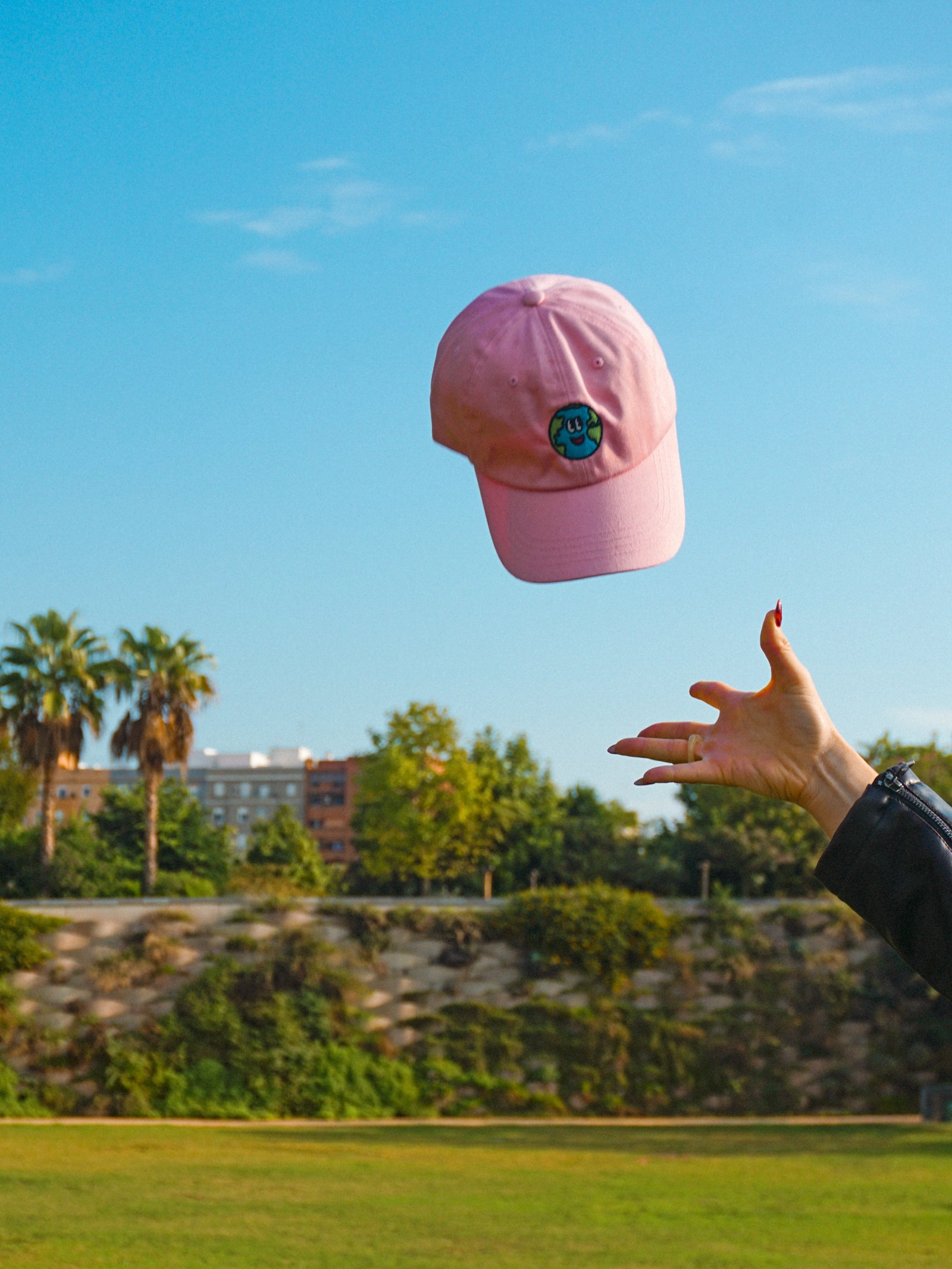 Pink cap being thrown in the air with a clear blue sky and trees in the background