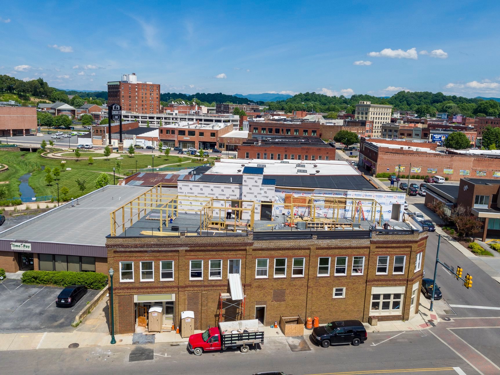 Aerial view of a town with a mix of buildings, green spaces, and a blue sky with clouds.
