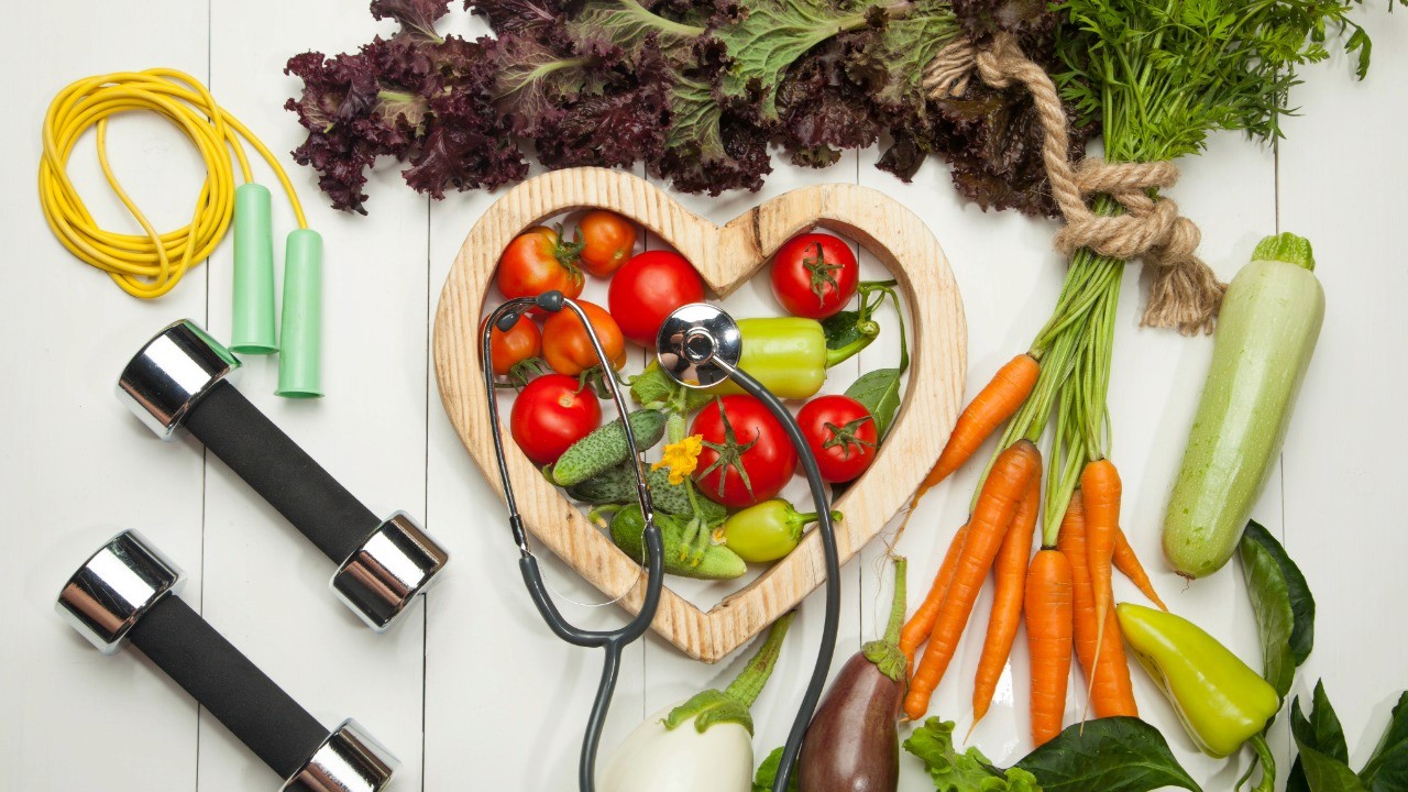 Vegetables in the shape of a heart surrounded by other vegetables and exercise equiptment