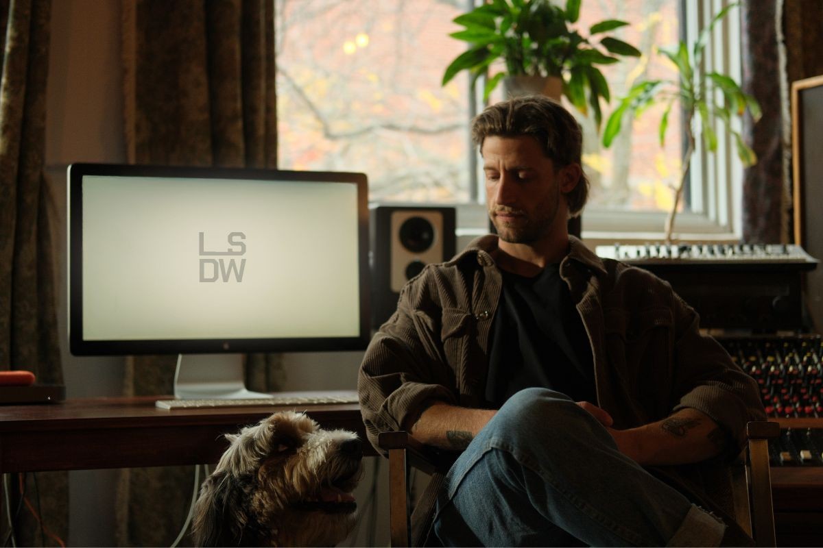 Personne assise dans un studio devant un écran affichant le logo LSDW, avec un chien à ses pieds