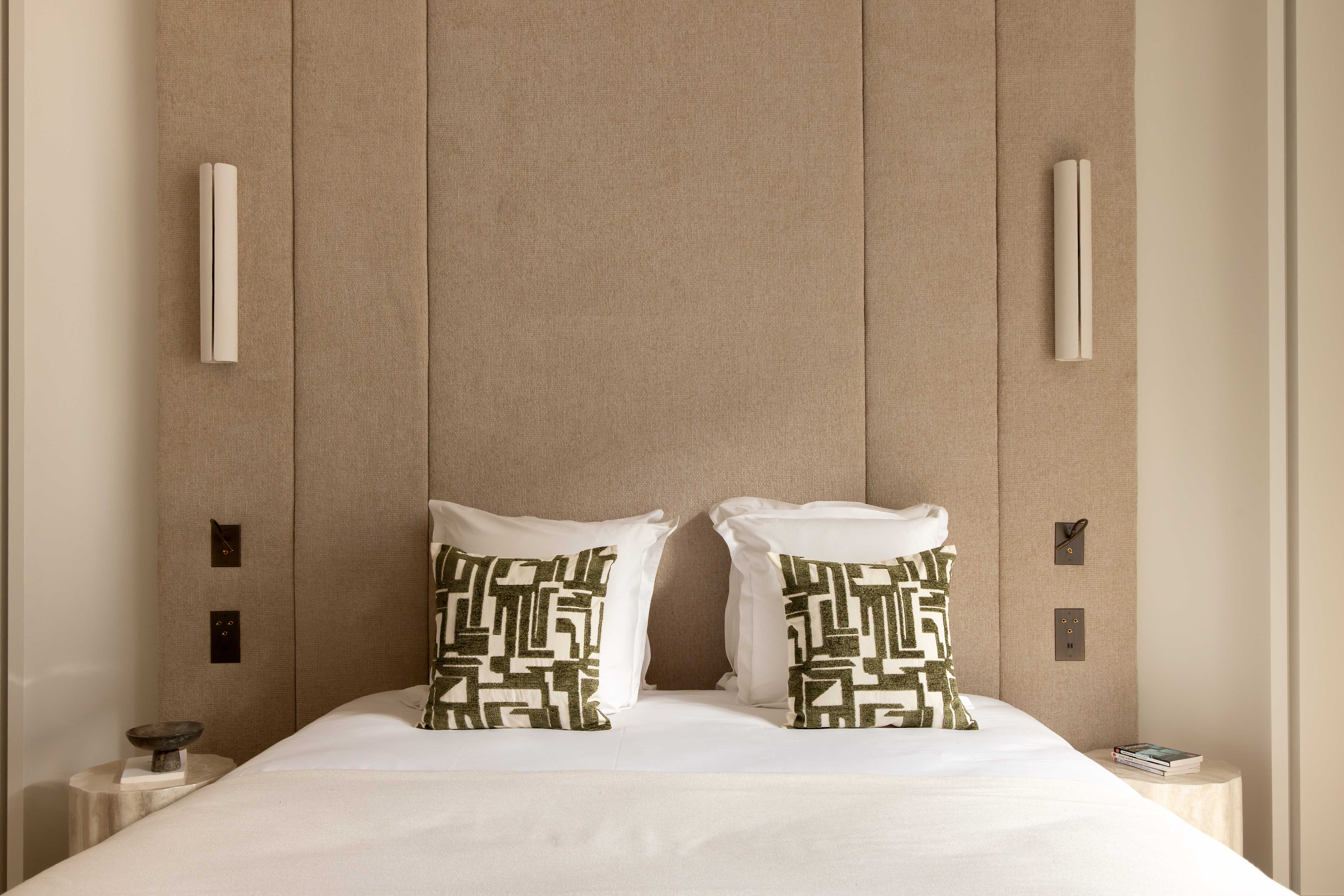 Lit double avec tete de lit sable en panneaux, coussins graphiques verts, appliques et chevets en travertin