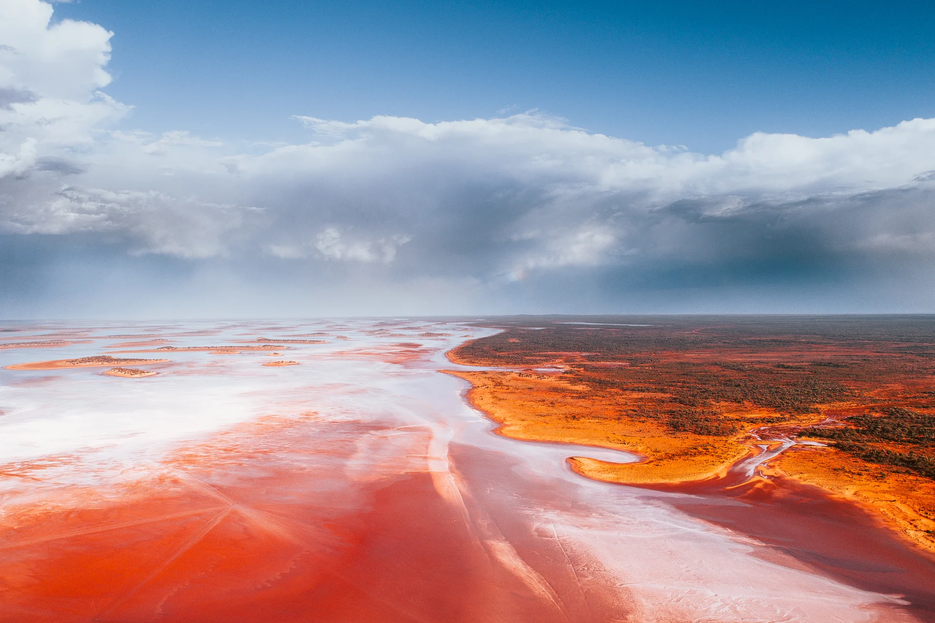 Aerial of pink and white salt flats stretching to a storm on the horizon
