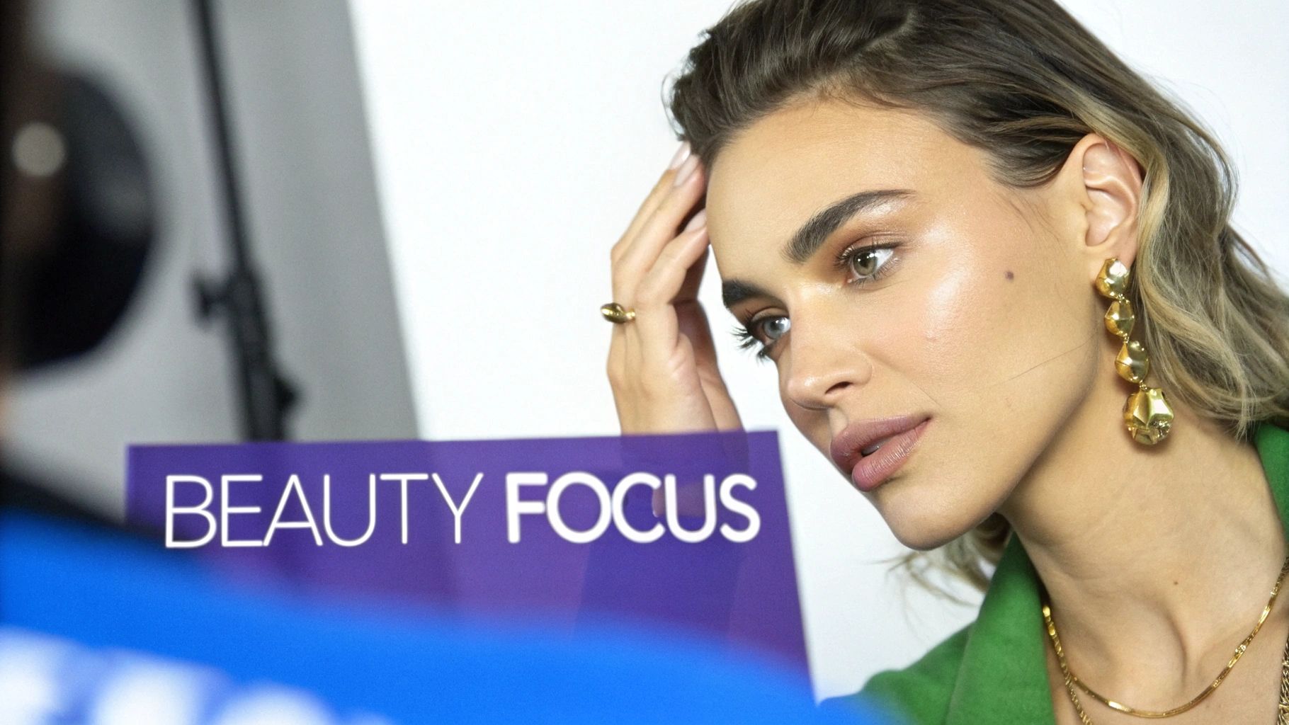 Close-up of a fashion model with makeup and gold jewelry, posing by a