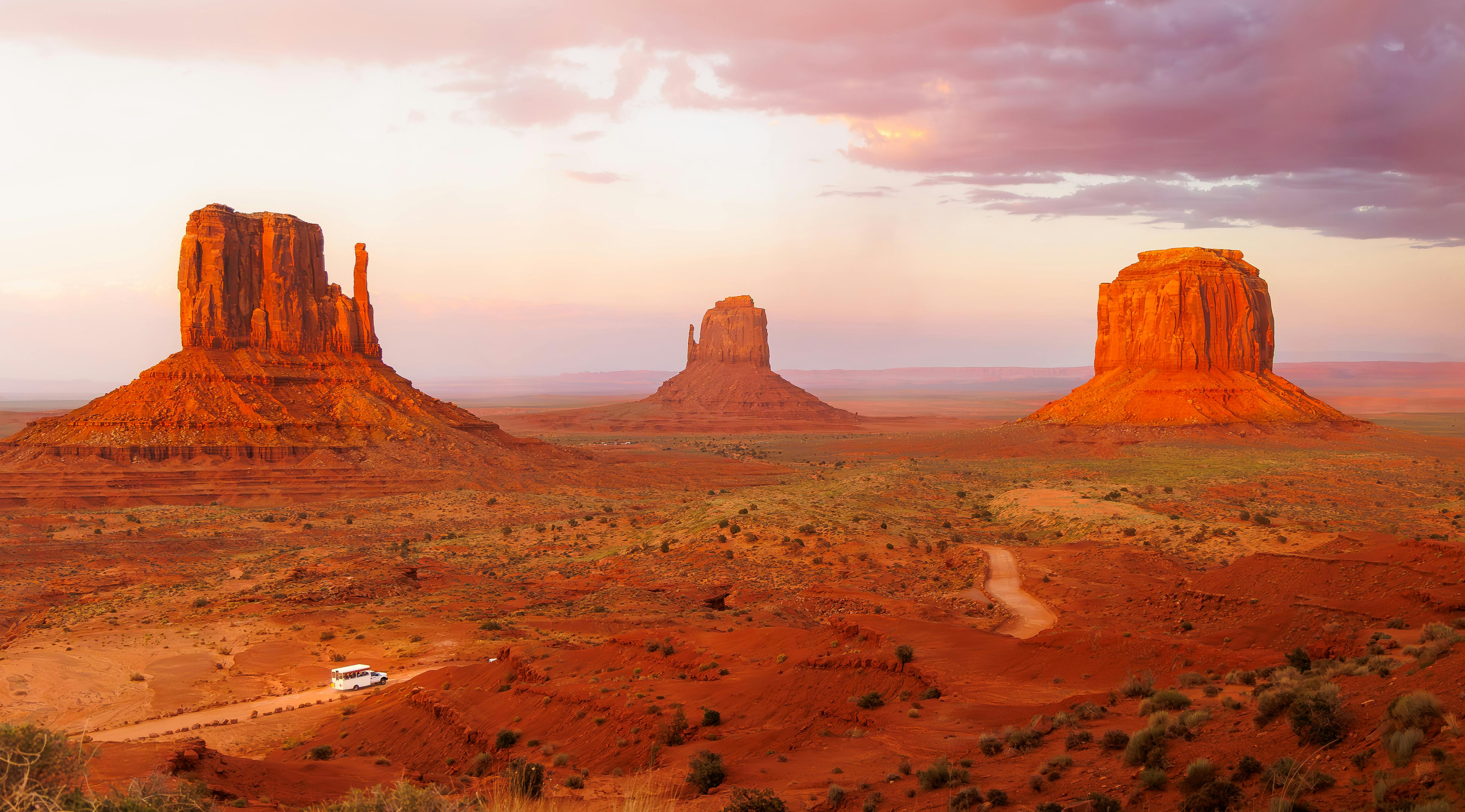 Three towering buttes stand majestically in a vast desert landscape under a colorful sunset sky.