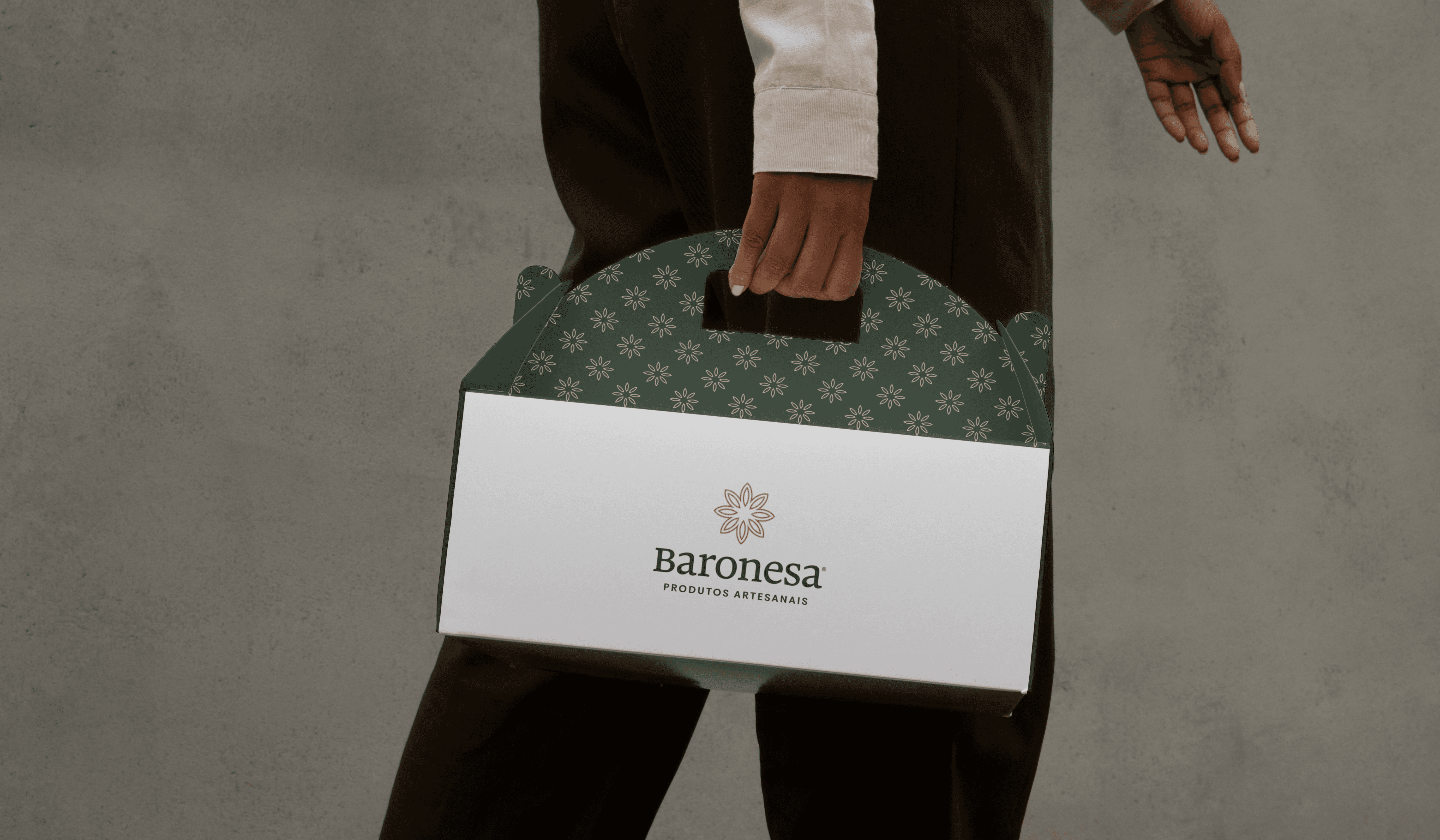 Pessoa segurando caixa de presente Baronesa com alça decorada em padrão floral verde, símbolo de tradição e elegância artesanal.