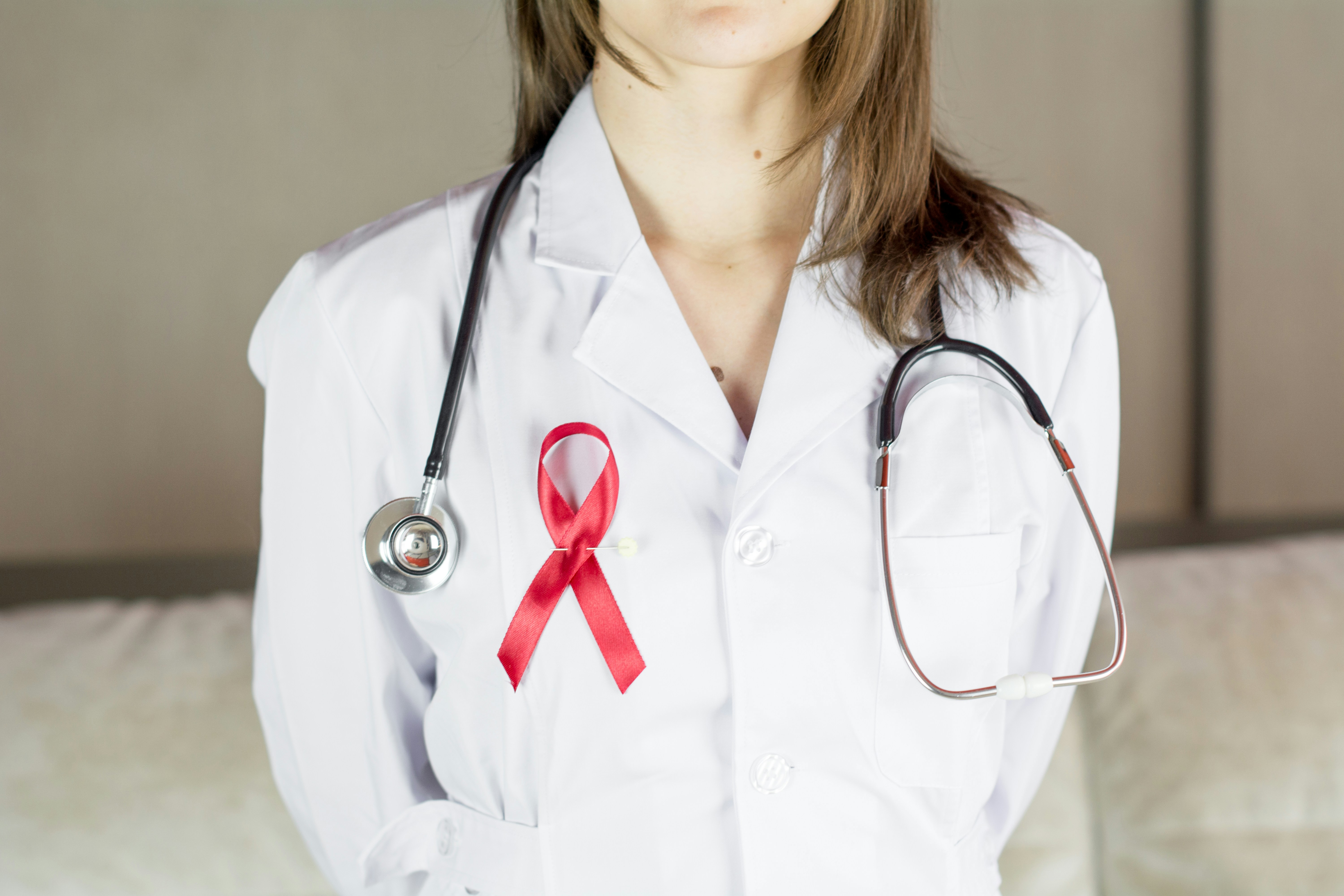 Person in a white lab coat with a stethoscope and a red awareness ribbon on the chest