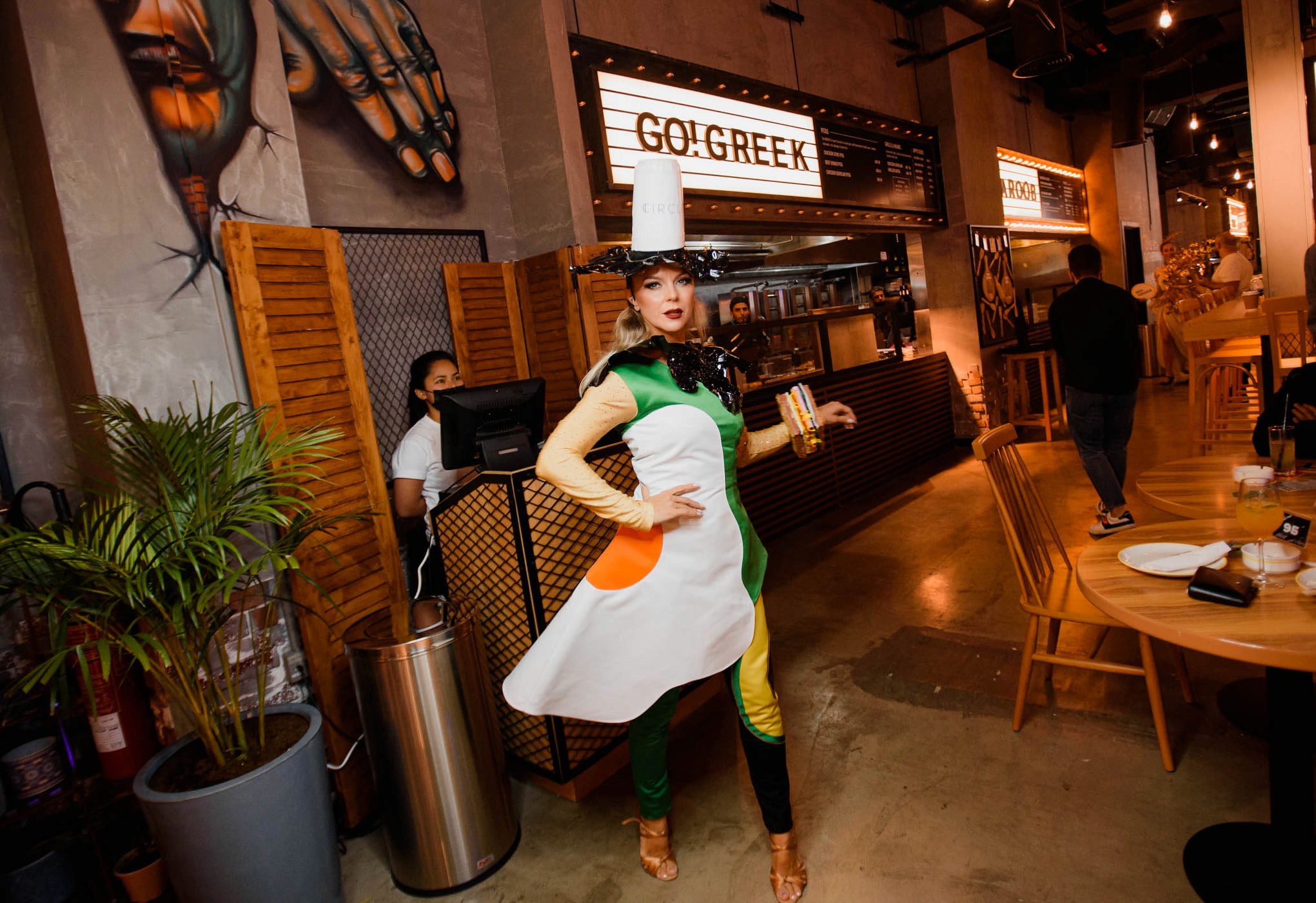 Performer entertaining guests inside a social restaurant with food stalls and communal seating.