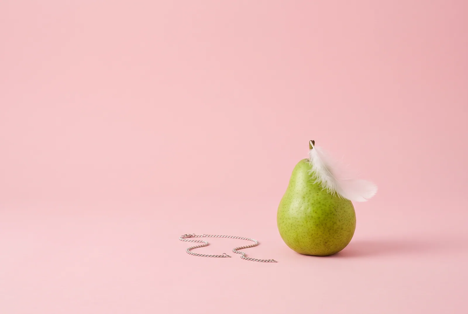 A broken silver chain beside a green pear with a white feather, Unchaind as a Christian app to quit porn