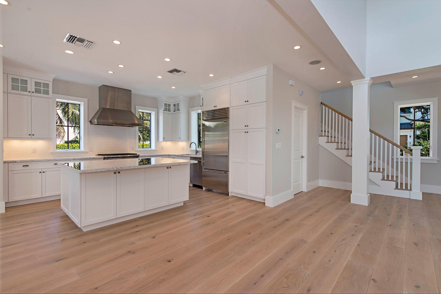 a large open room with a kitchen on the left side that showcases a center island and white cabinets