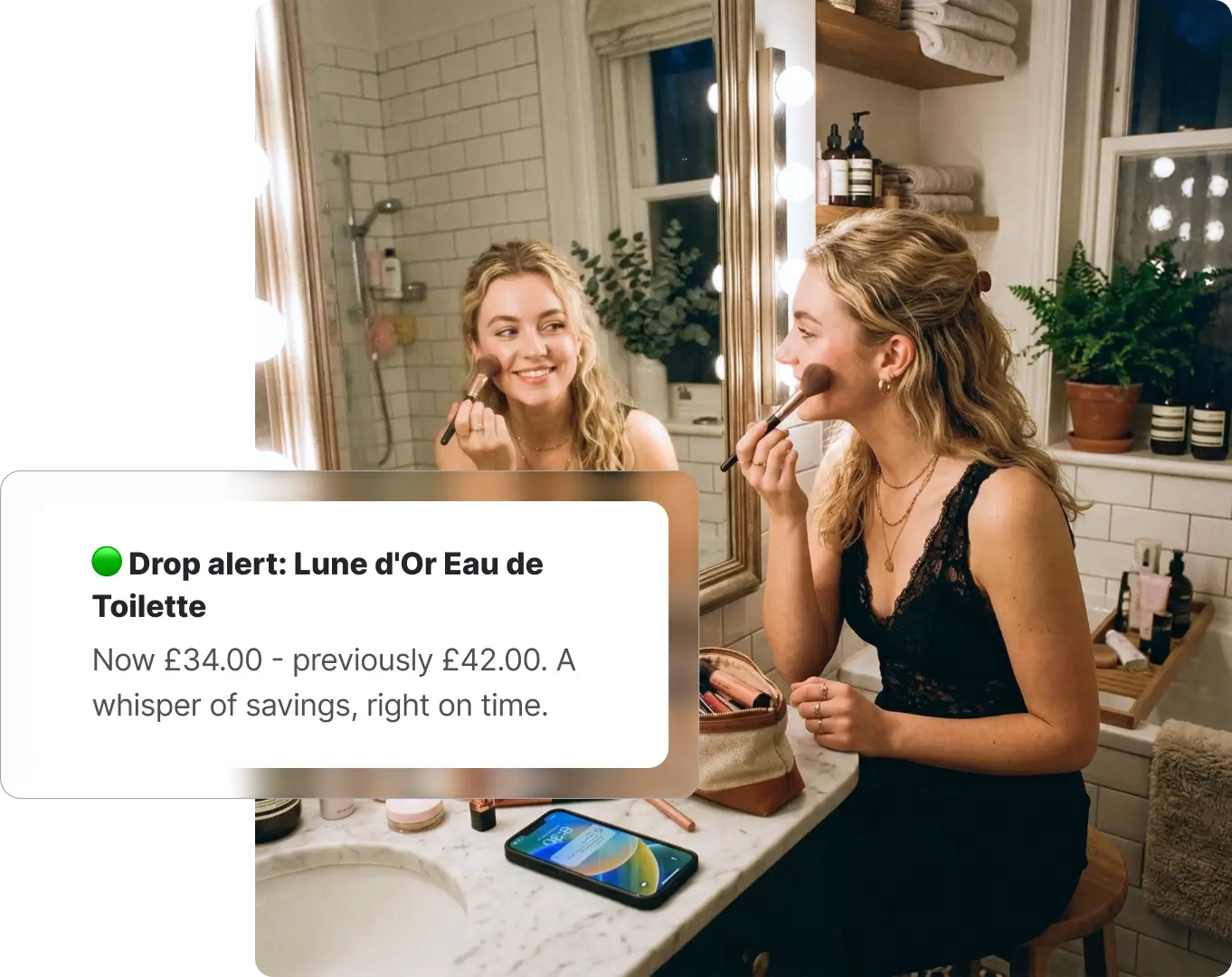 Woman getting ready in front of a bathroom mirror with warm lighting, with a Whisprice drop alert notification overlaid showing a price drop on a SereneGlow Ultrasonic Essential Oil Diffuser from £42.00 to £34.00.
