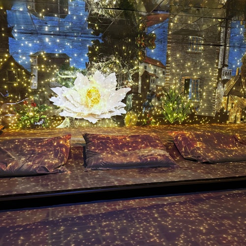 Three cushions on a floor with a background of a glowing flower, buildings, and twinkling lights.