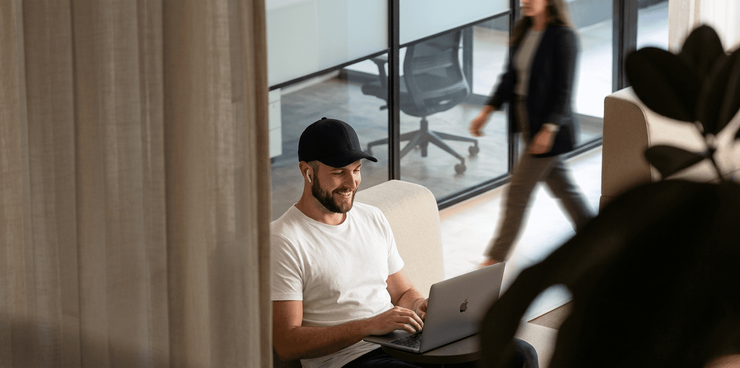 man in a black cap talking to a woman at a computer in a meeting room