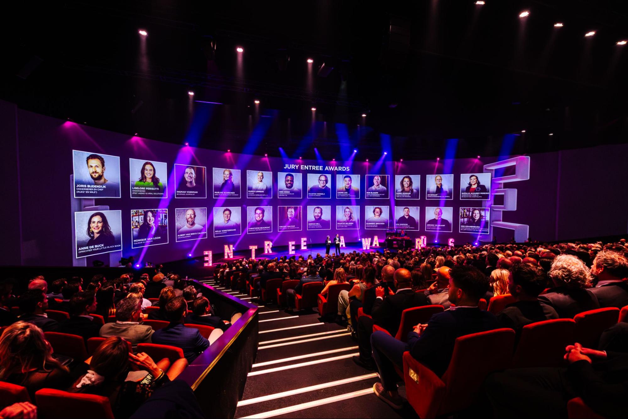 foto van volle Theaterzaal met foto's op groot scherm