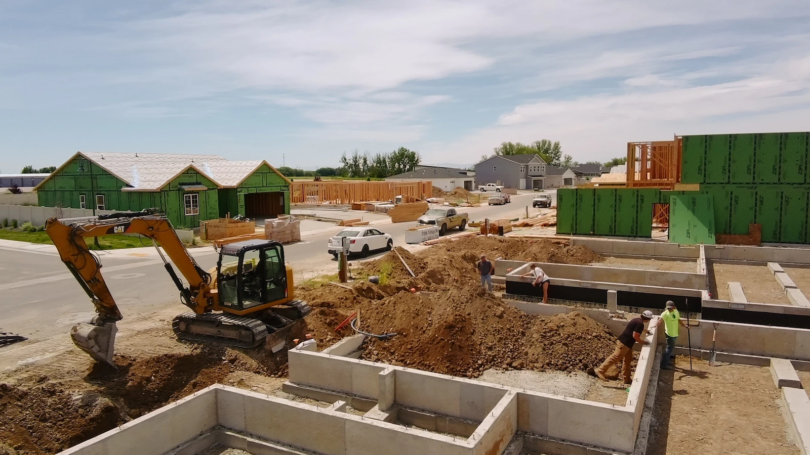 A yellow Caterpillar excavator and several workers build concrete foundations at a residential development.
