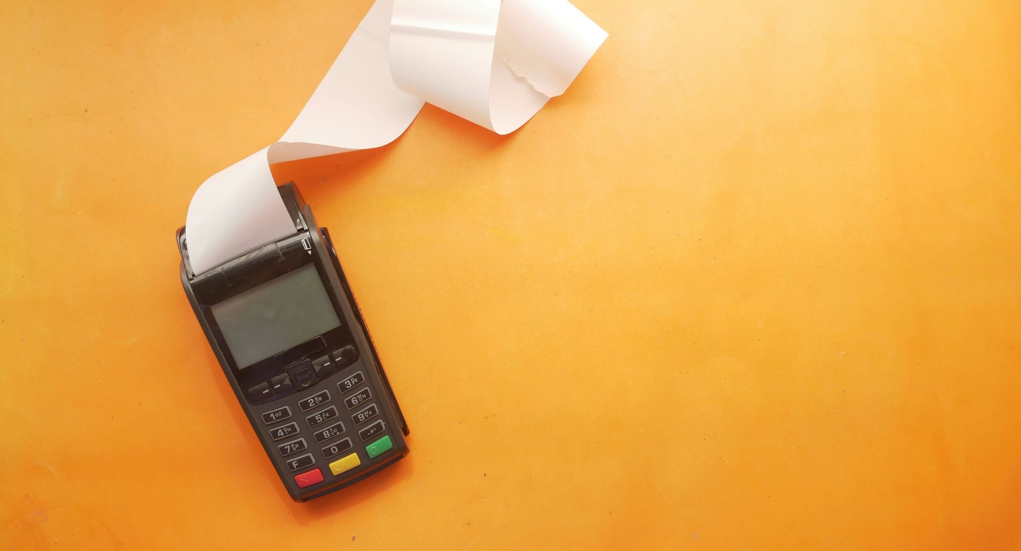maquininha de cartão com notinhas em branco saindo dela, fundo laranja