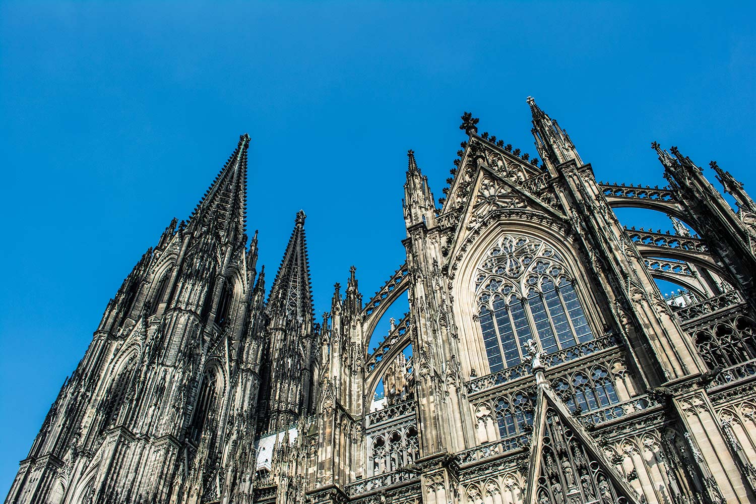 Low-angle view of the ornate Gothic spires and stone facade of a cathedral against a clear blue sky.