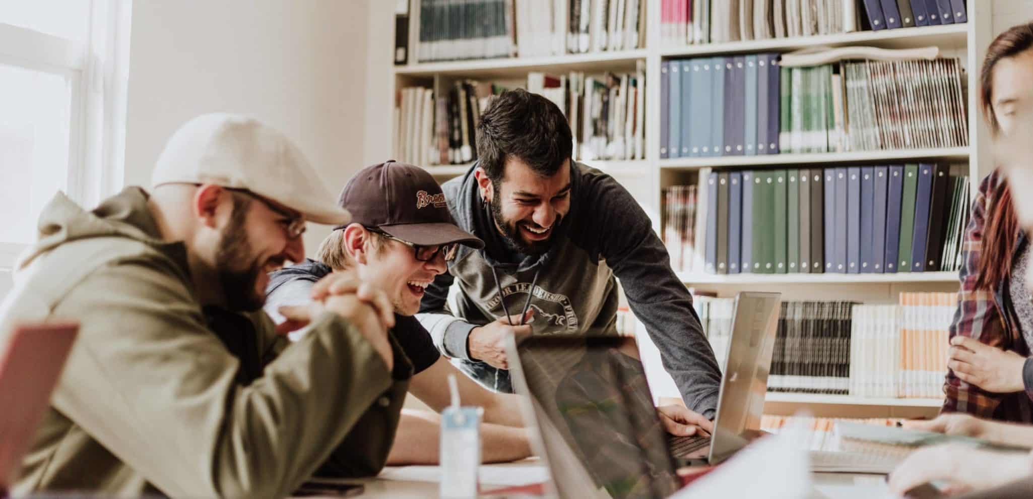 Team collaboration in a library, group of people laughing and working on laptops.