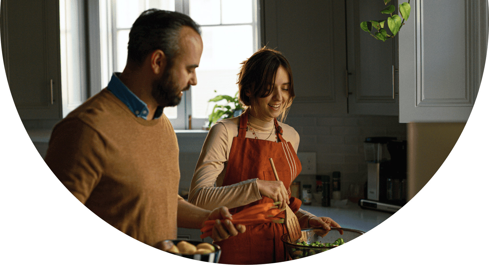 A man and woman are cooking together in a bright kitchen, sharing a joyful moment while preparing a meal.