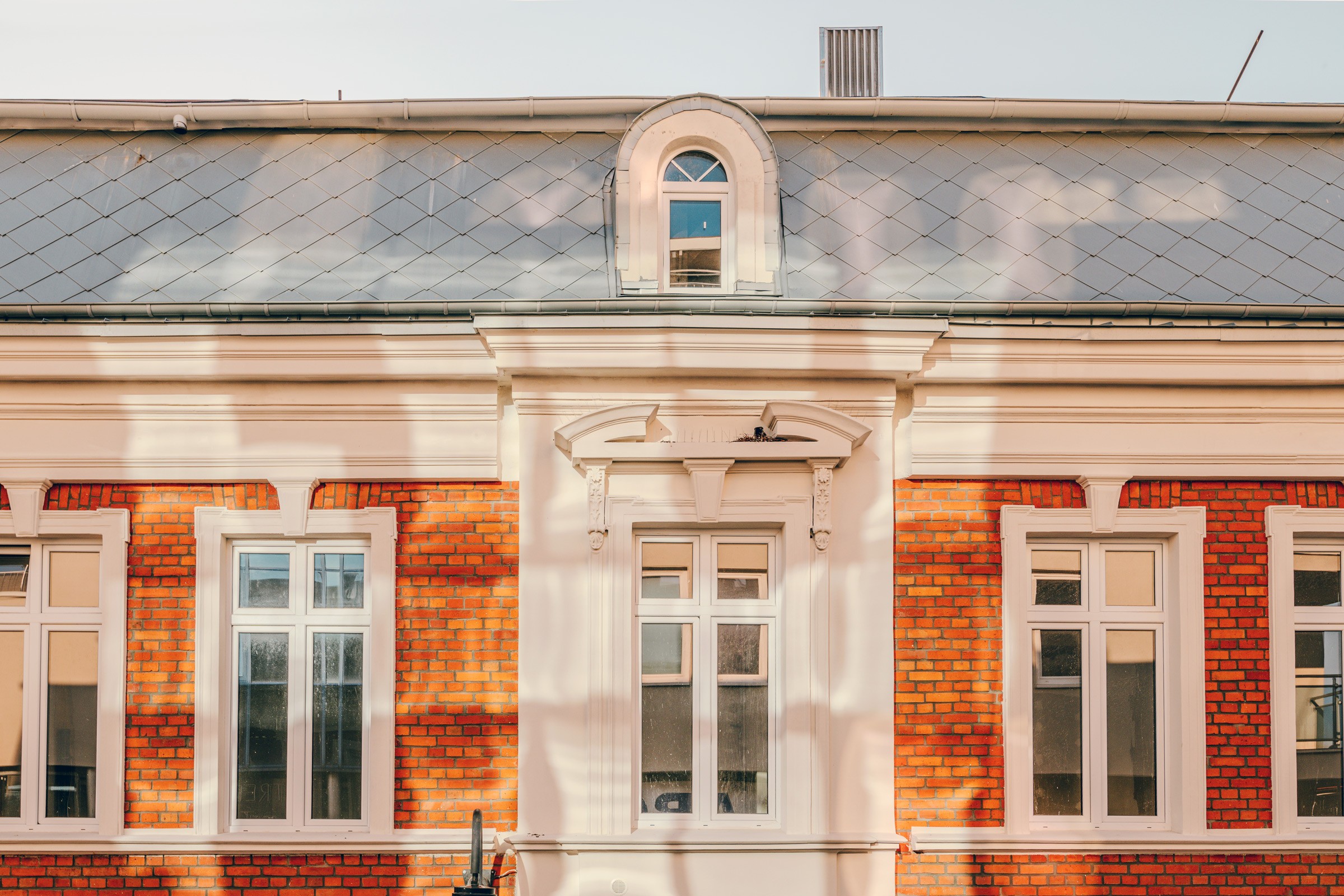 Piękny budynek w stylu klasycystycznym z czerwonymi cegłami. Na rogu ulicy z białymi elementami. Detal fasady z oknami i czerwoną cegłą.