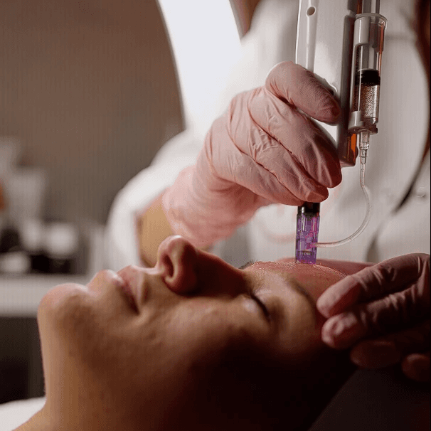 Portrait of a woman with short brown hair, eyes closed, gently touching her face with both hands against a beige background