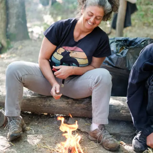 donna in esperienza di sopravvivenza indigena, seduta accanto al fuoco in connessione con la natura