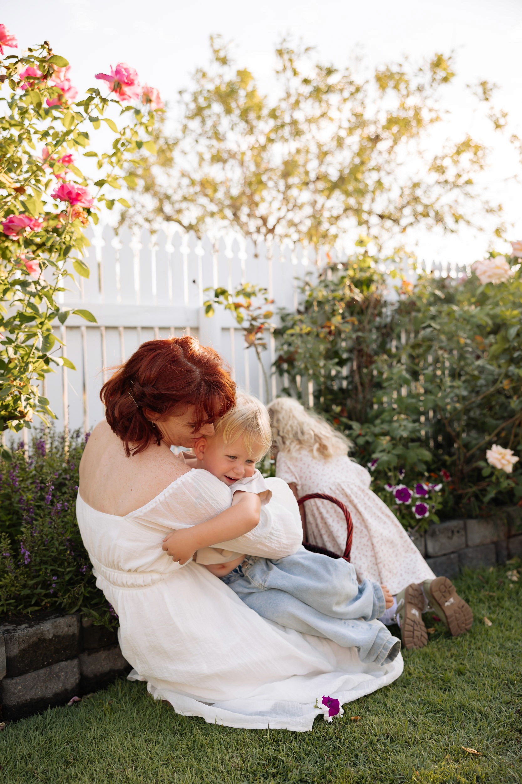Mother holding her child in sunlit flower garden in home photography session in Mackay