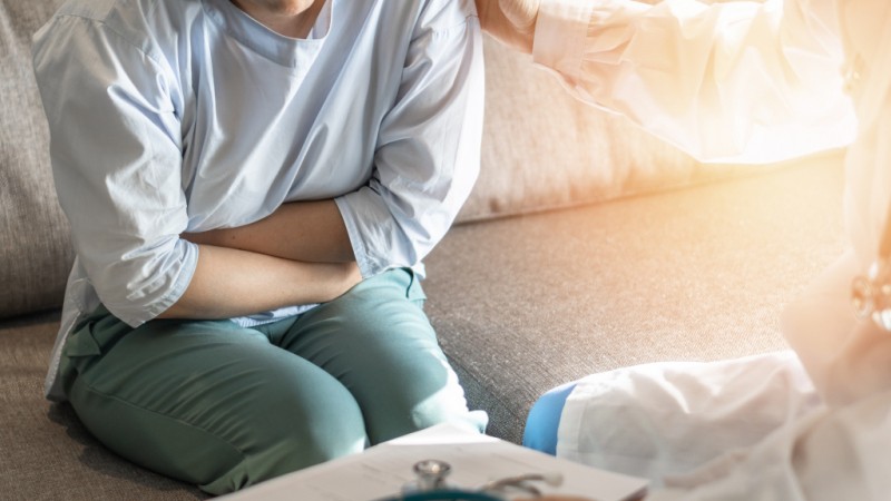 Nurse holding a female reproductive system model while discussing test results with a patient in a clinic.