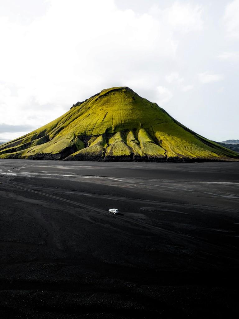 A car traveling on a dirt road with a green mountain in the background