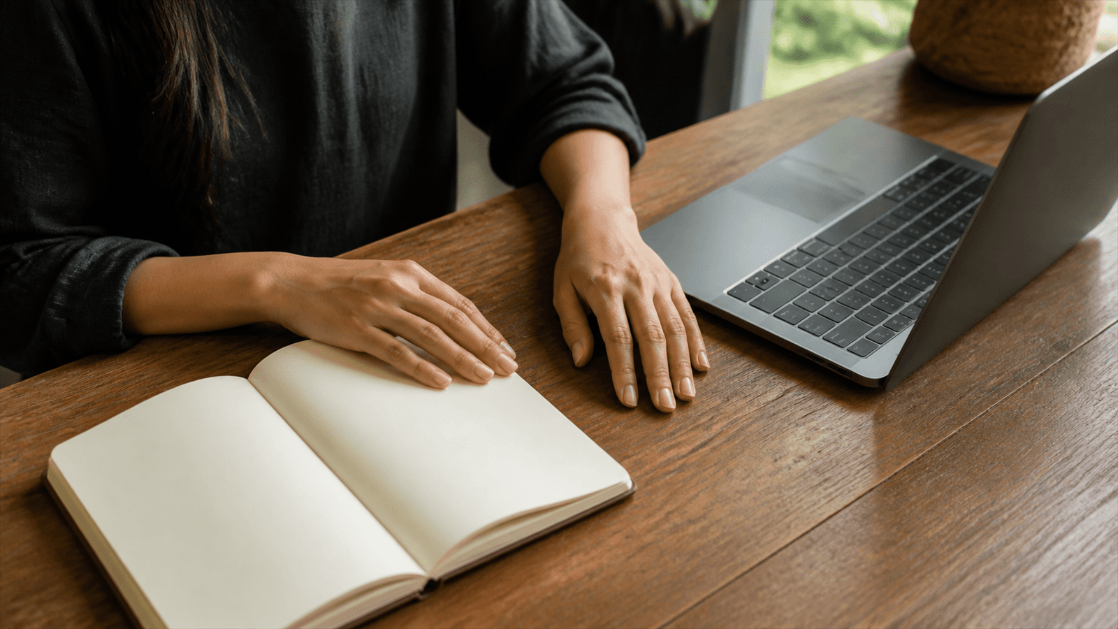 A woman's hands rest beside a laptop during a quiet pause between work tasks.
