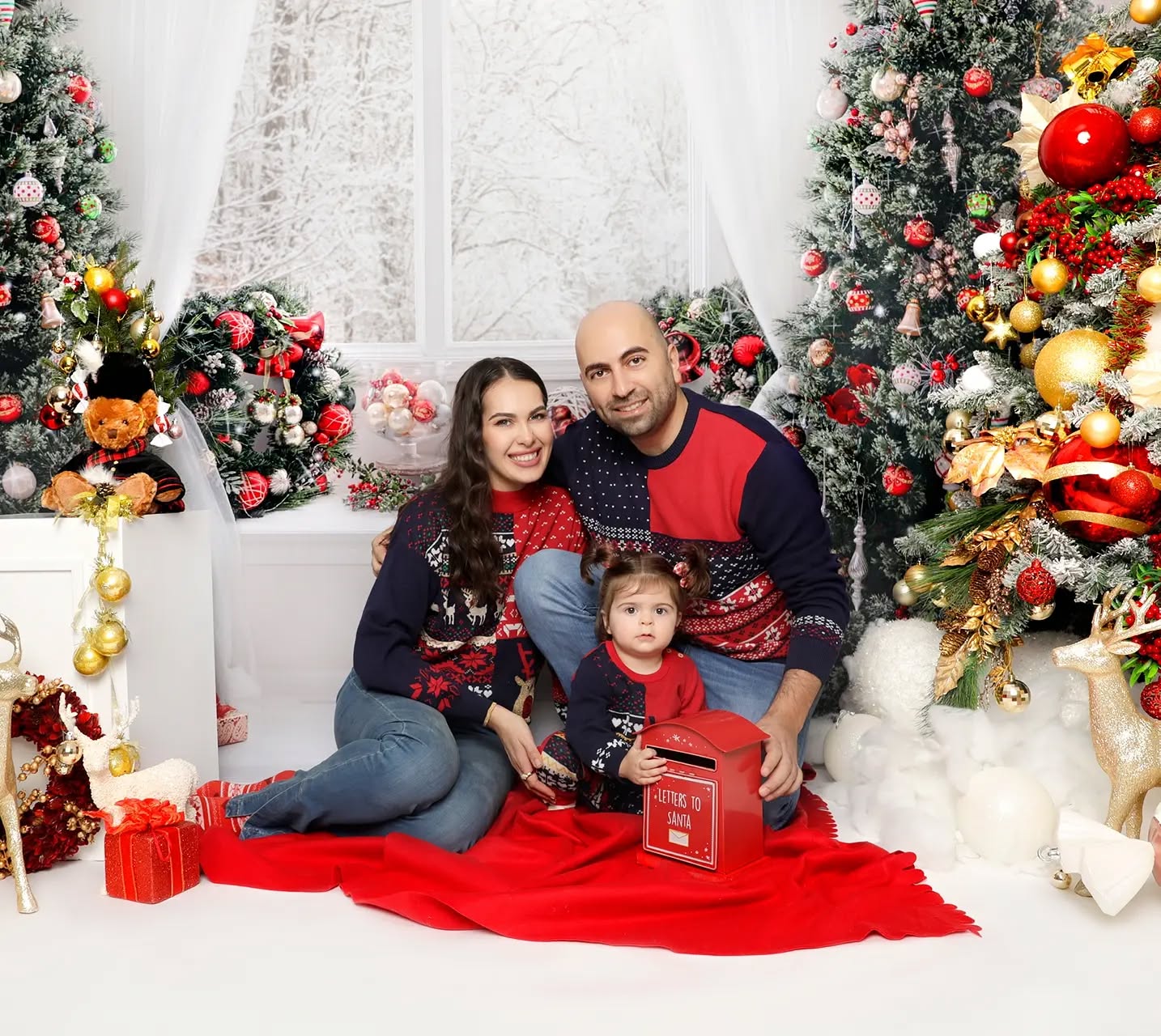 A family of three seated, beautifully photographed in a creative Christmas family photoshoot set up at Mahvin Photography studio.