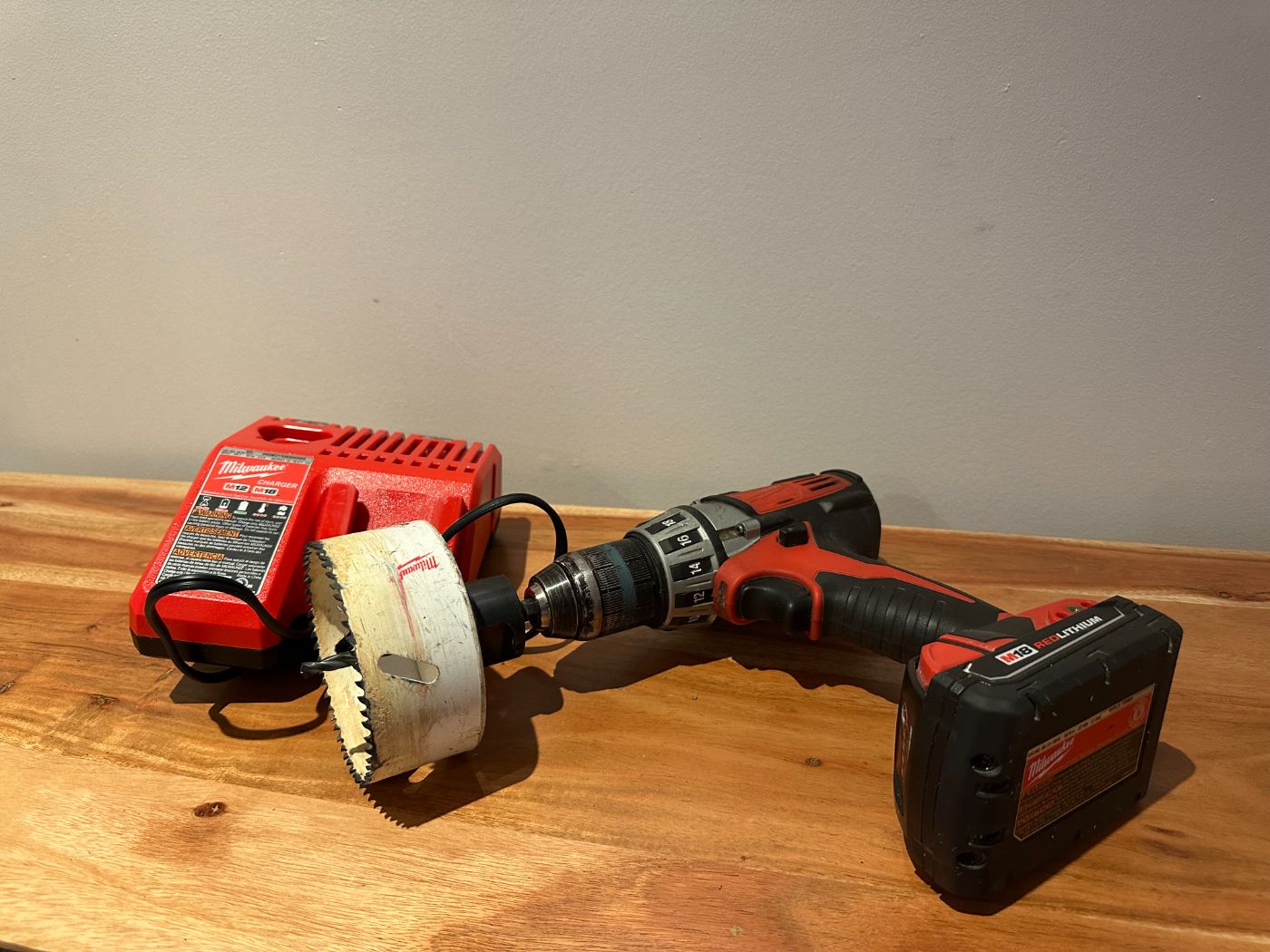 Perceuse-visseuse sans fil Milwaukee M18 avec scie cloche de 4 pouces et chargeur, posée sur une table en bois à Montréal – Saint-Henri