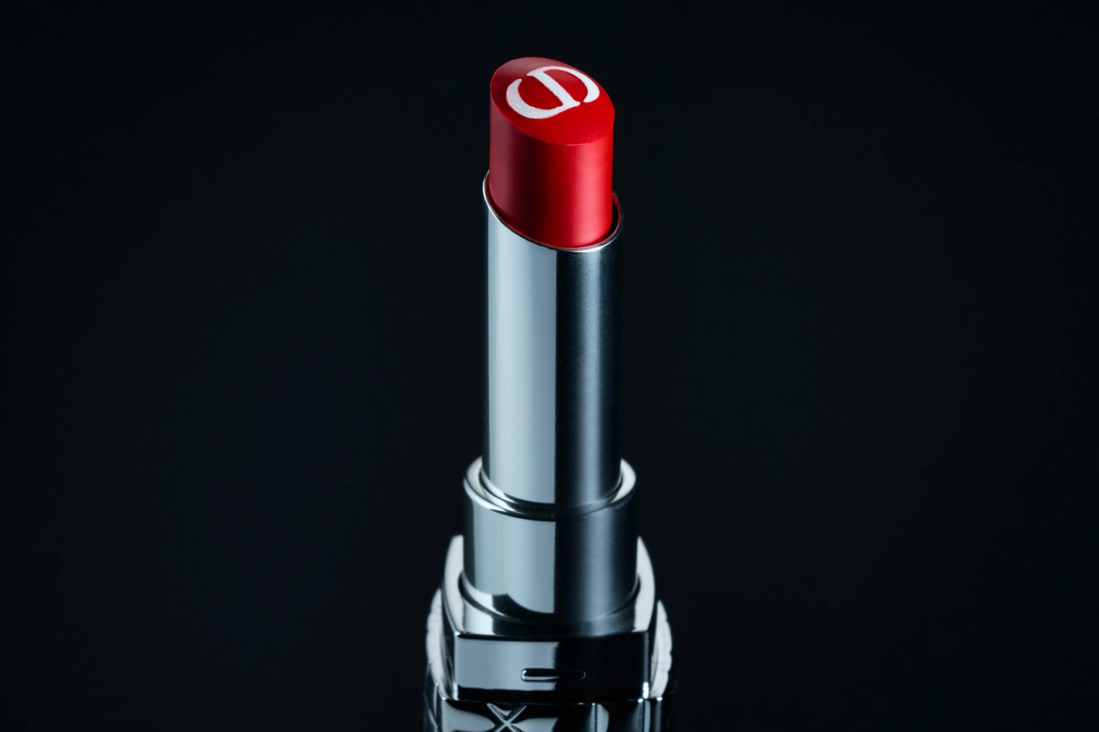 A close-up of a lipstick tube with a shiny red top against a dark background.