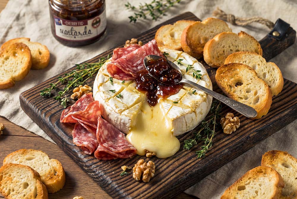 Baked brie appetizer with cured meat and cherry fig mostarda.