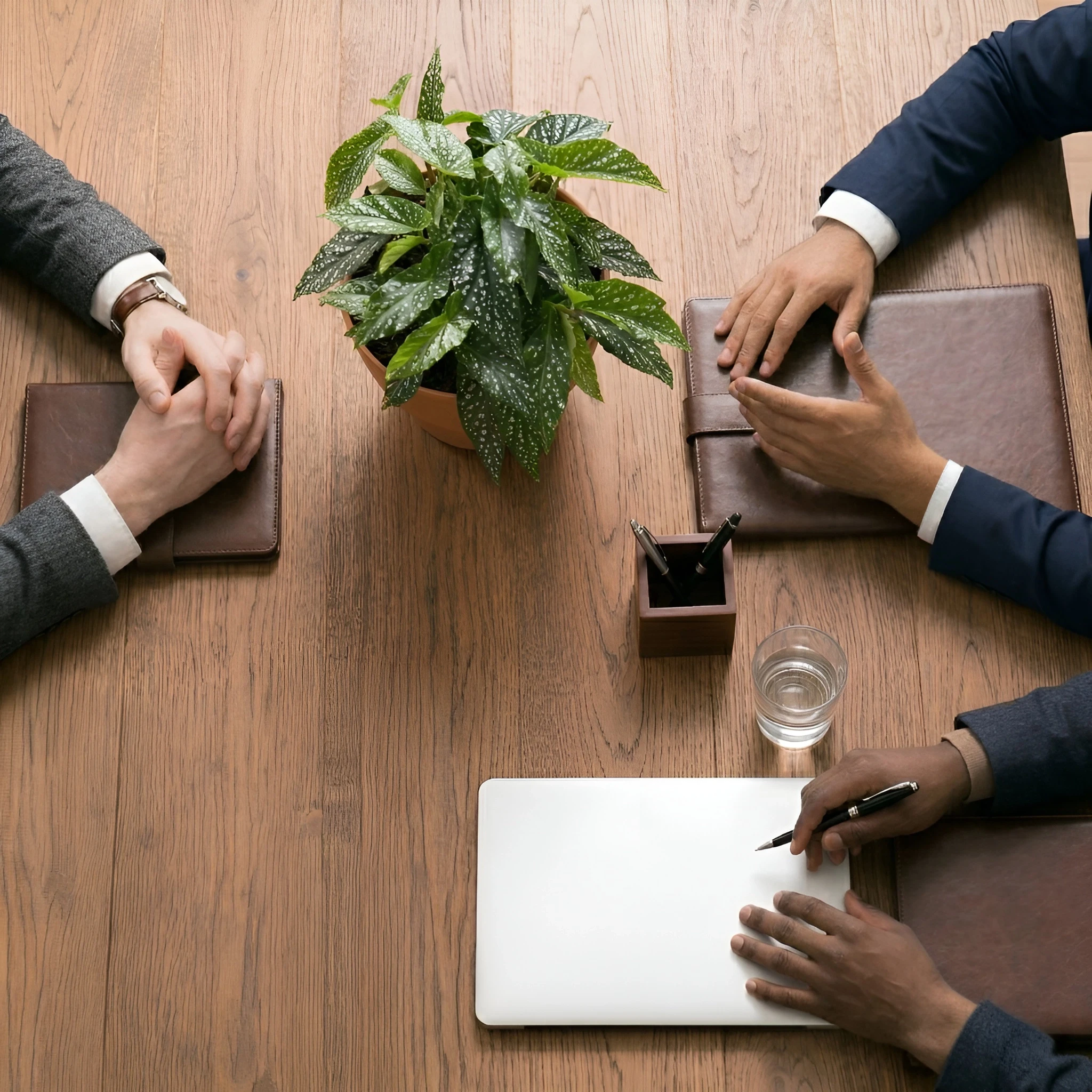 Top-down view of three professionals in suits sitting at a wooden table with notebooks and a laptop.