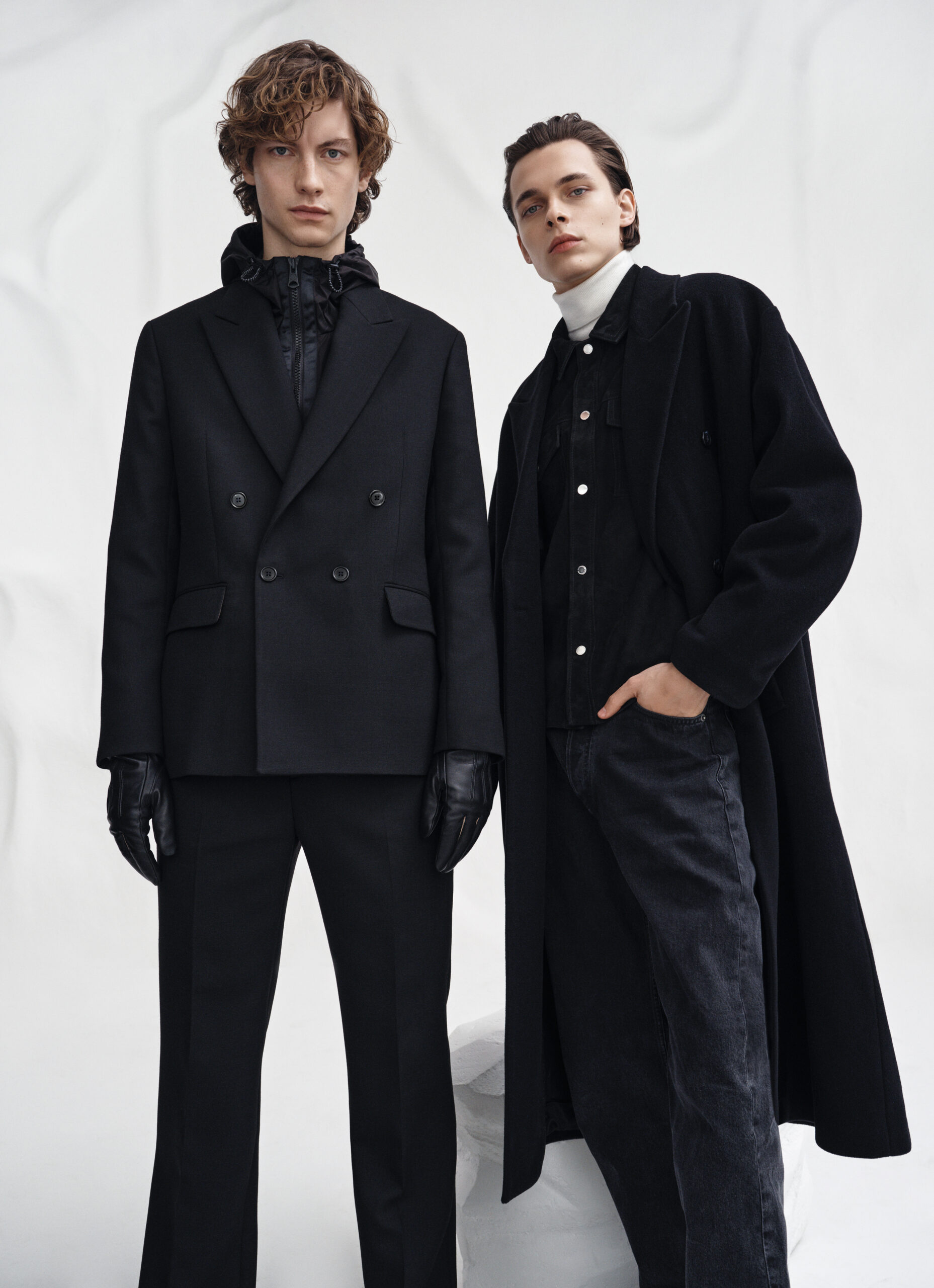 Two models in black outerwear against the sculpted white FW21 set