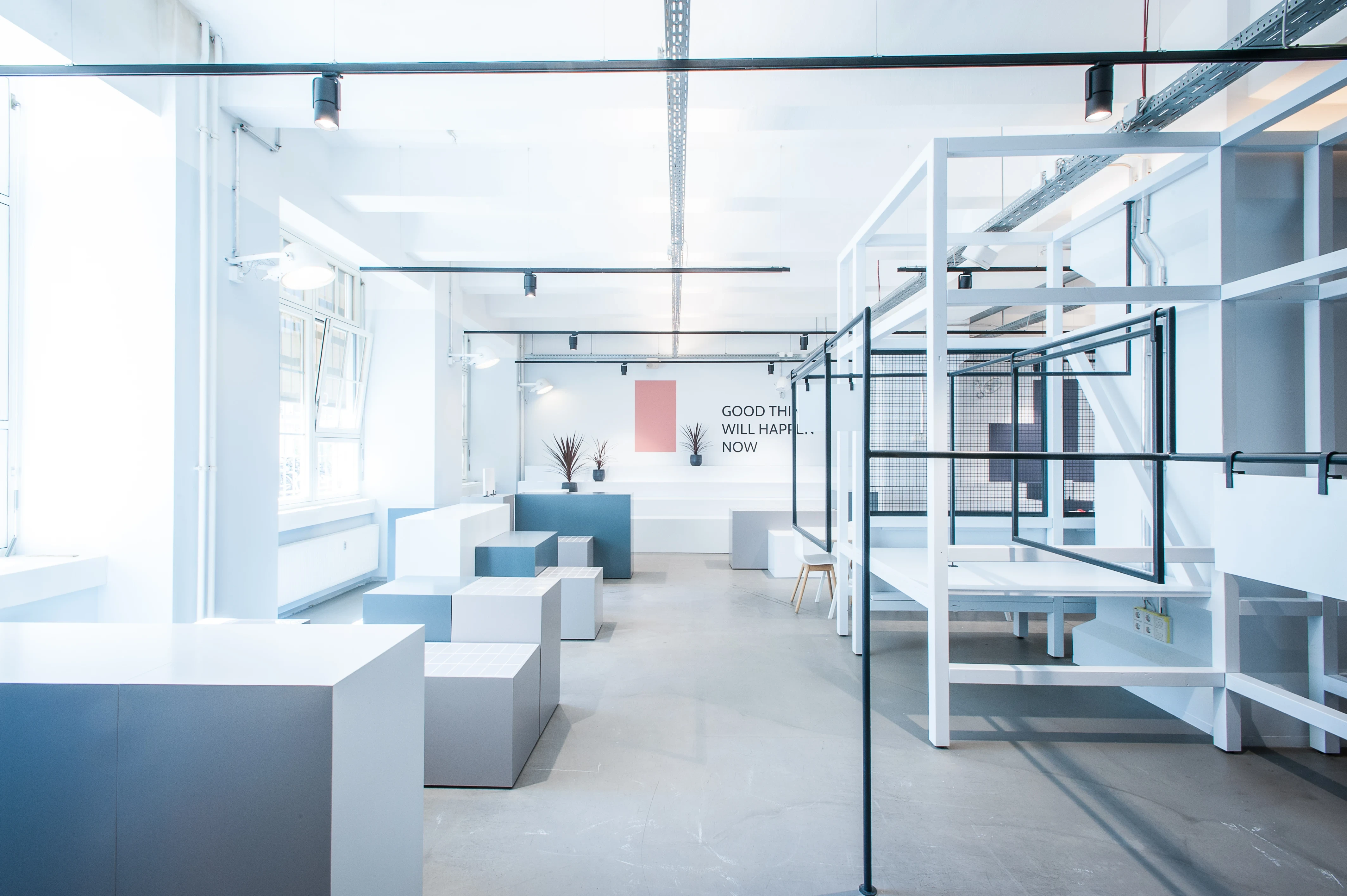 Bright showroom for 17 FASHION BRANDS with white and blue-grey display cubes, white steel rack structures with black clothes rails and the slogan Good Things Will Happen Now on the wall.