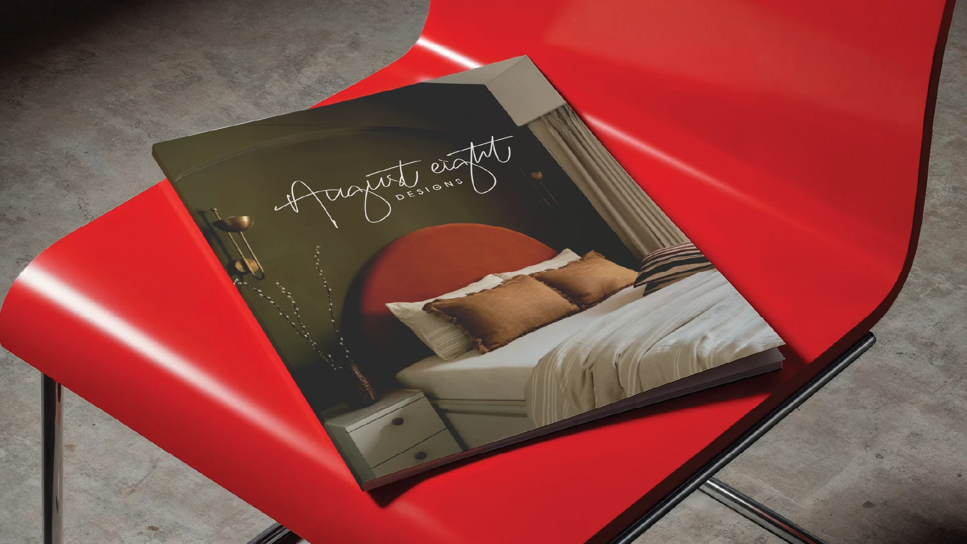 A red chair holds a modern design magazine featuring a stylish bedroom with earth-toned decor on its cover.