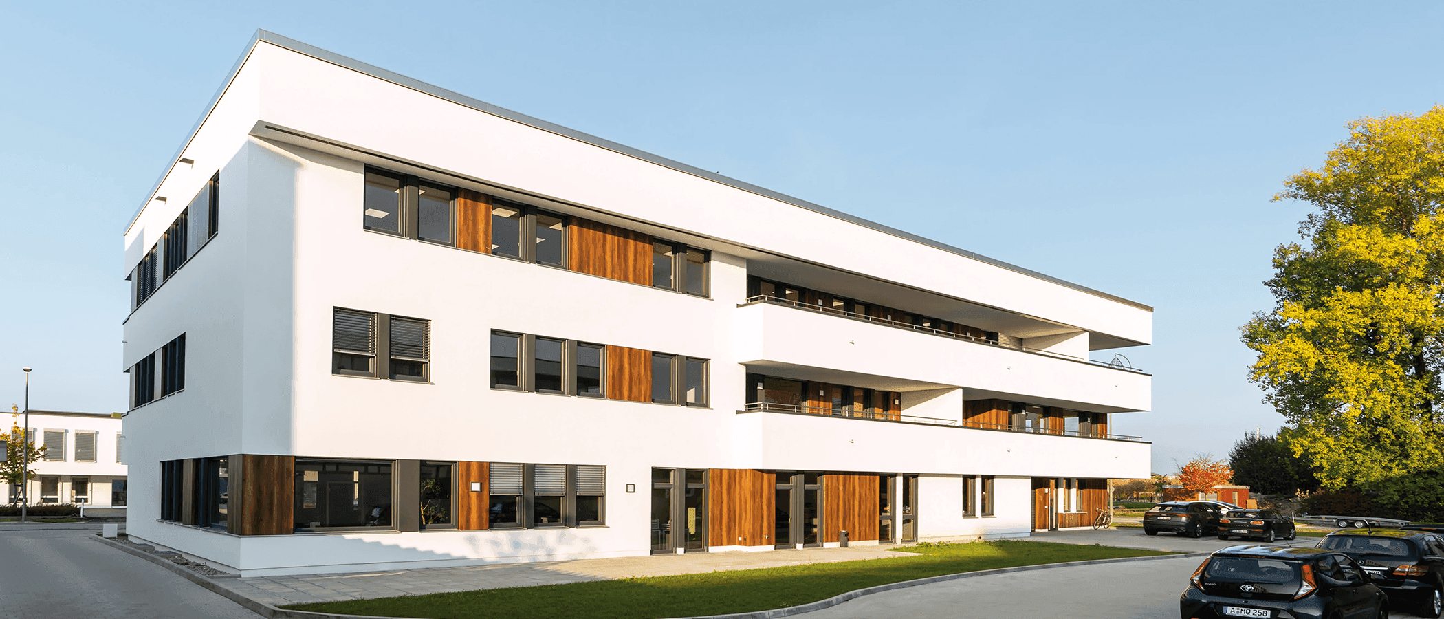 Blick auf modernes Bürogebäude mit Parkplatz davor.