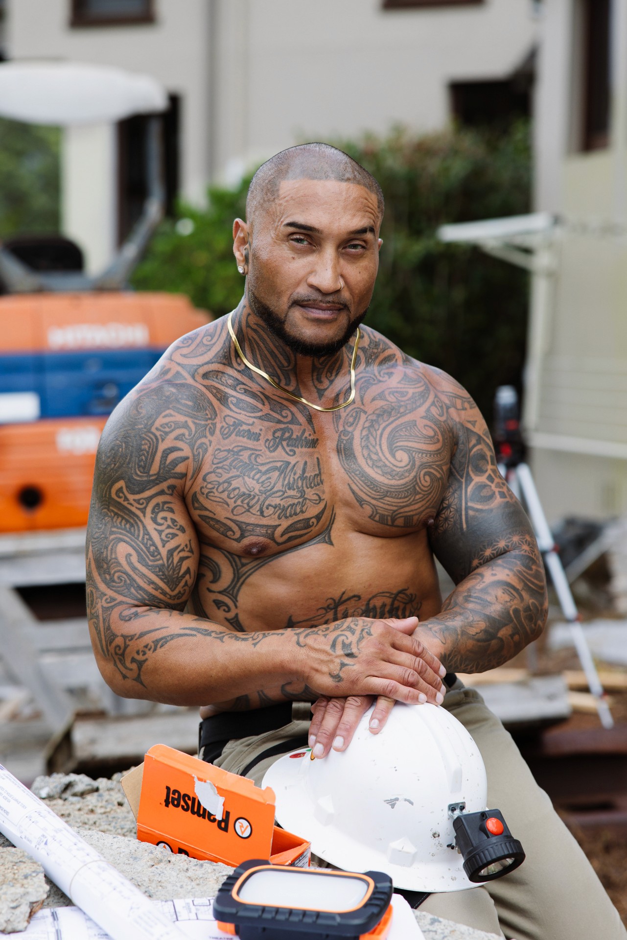 Shirtless surveyor sitting with hands on hard hat