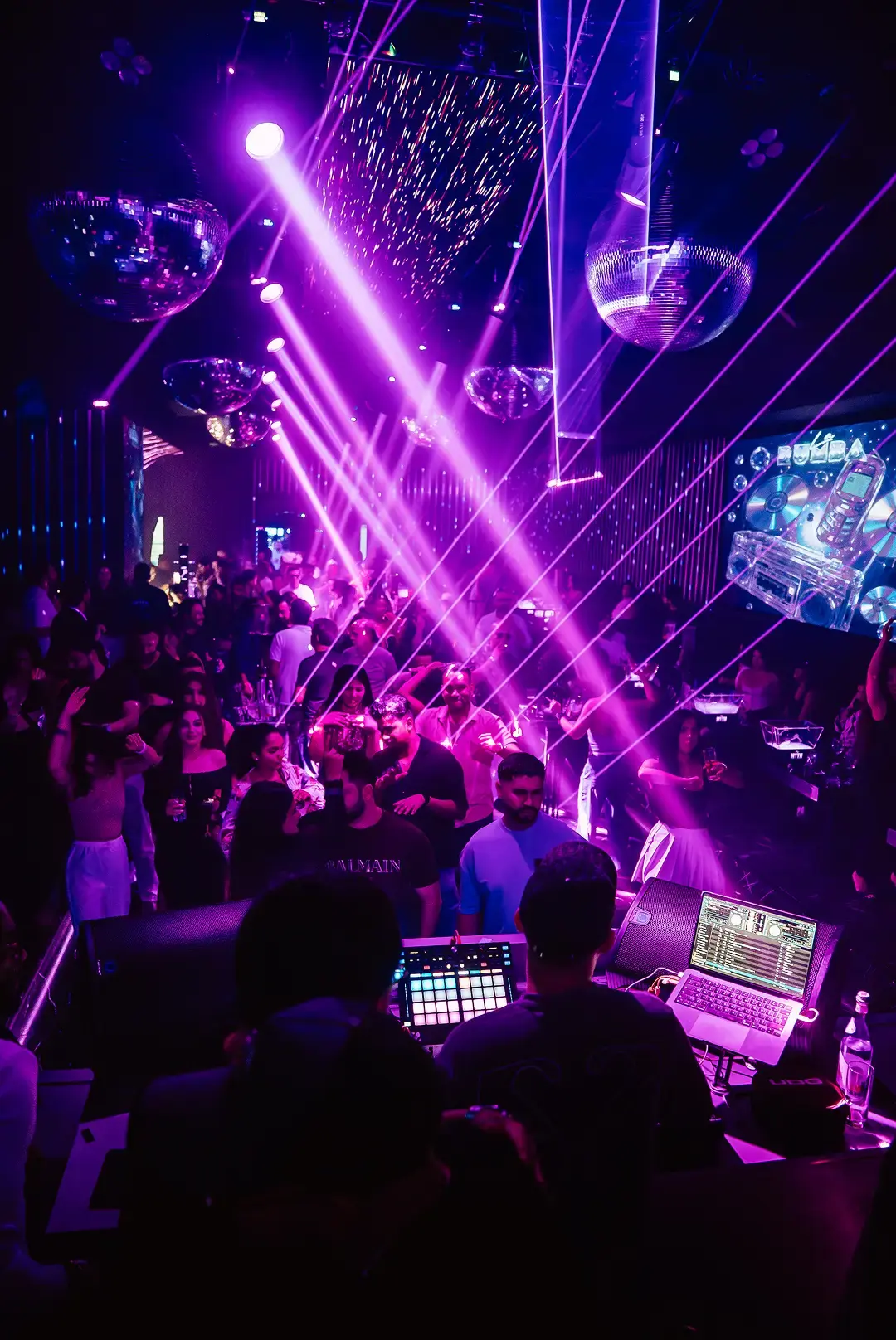 View from the DJ booth over a packed dance floor at The Myth Dubai, with purple lasers, disco balls and La Rumba visuals
