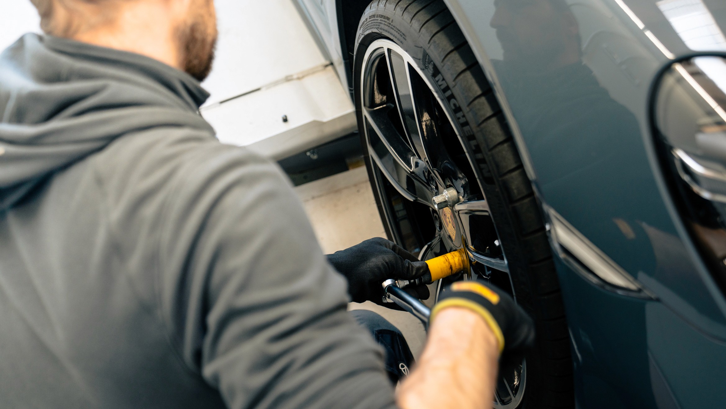 Mechaniker beim Reifenwechsel an einem Auto – Nahaufnahme eines Fachmanns, der mit einem Werkzeug Radschrauben anzieht. Fokus auf das Rad und die Hände in Arbeitshandschuhen.