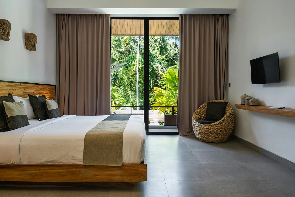 Deluxe sea view room with a large bed, tropical greenery outside, and a cozy seating corner.