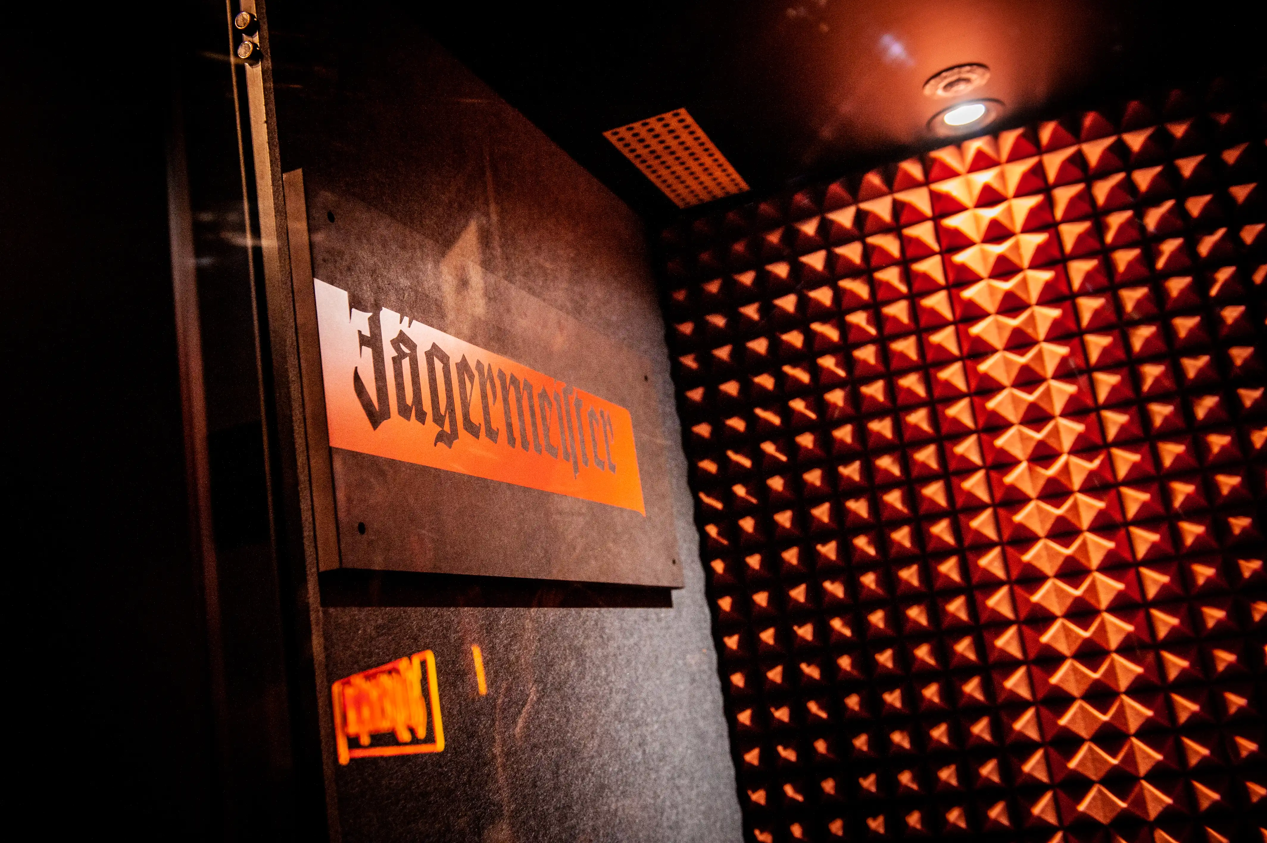 Door with orange Jägermeister sign opening into a small booth lined with orange-lit pyramid acoustic foam at JÄGERMEISTER x SVENNI'S.