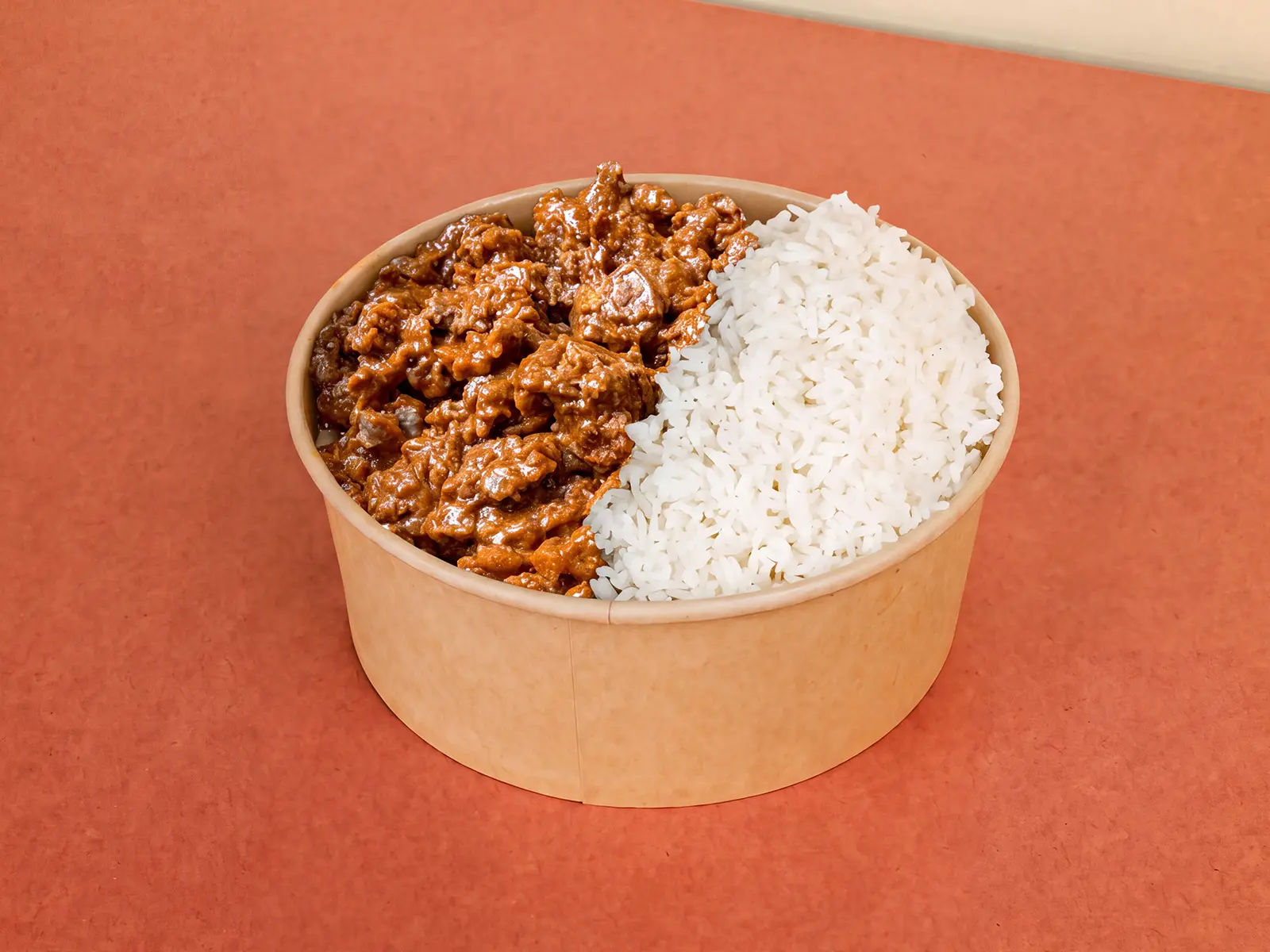 A takeout bowl divided between fluffy white rice and seasoned minced beef, photographed on a warm orange-red surface.