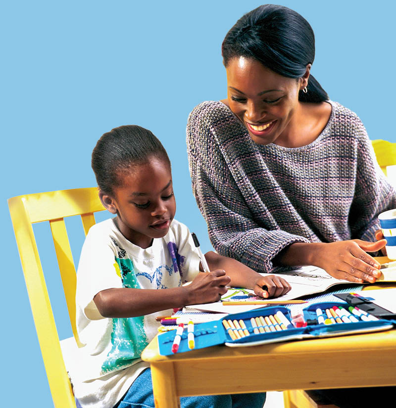 Adult and child sitting at a small table, coloring together with markers and art supplies, against a light blue background