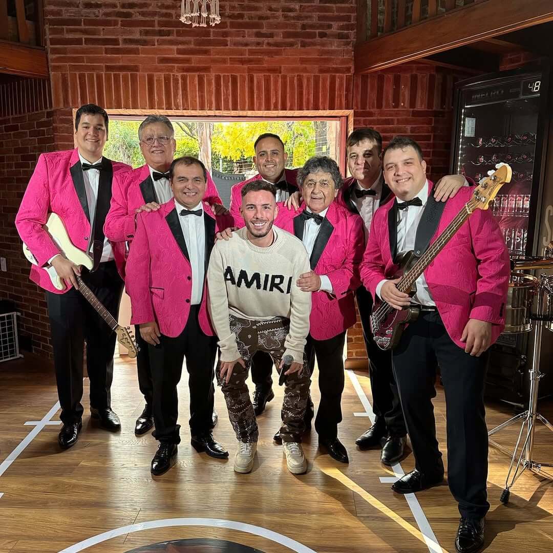 Fer Palacio con una banda de cumbia vestidos de rosa, posando antes de un show.