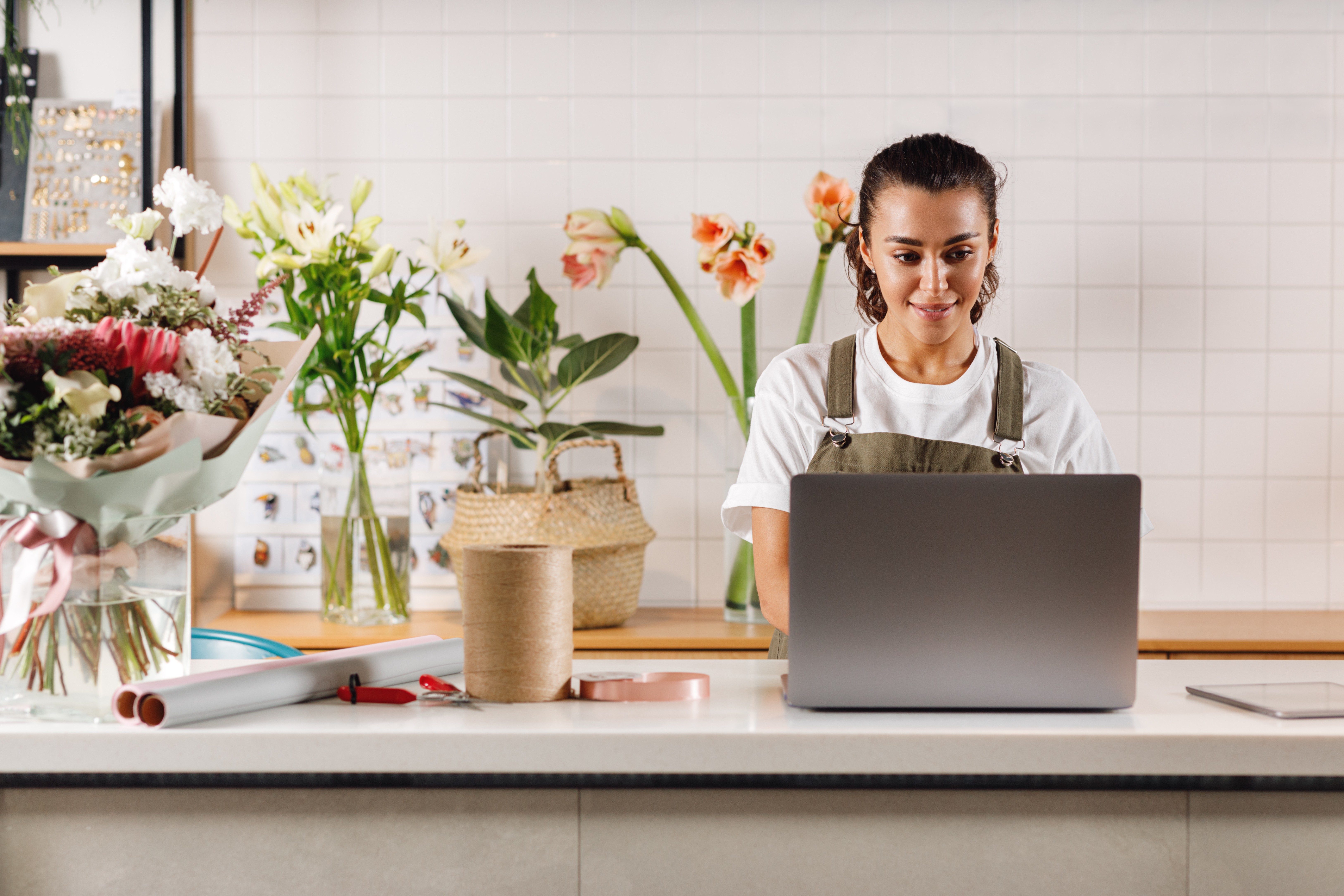 Woman working on a laptop surrounded by fresh flowers in a small flower shop