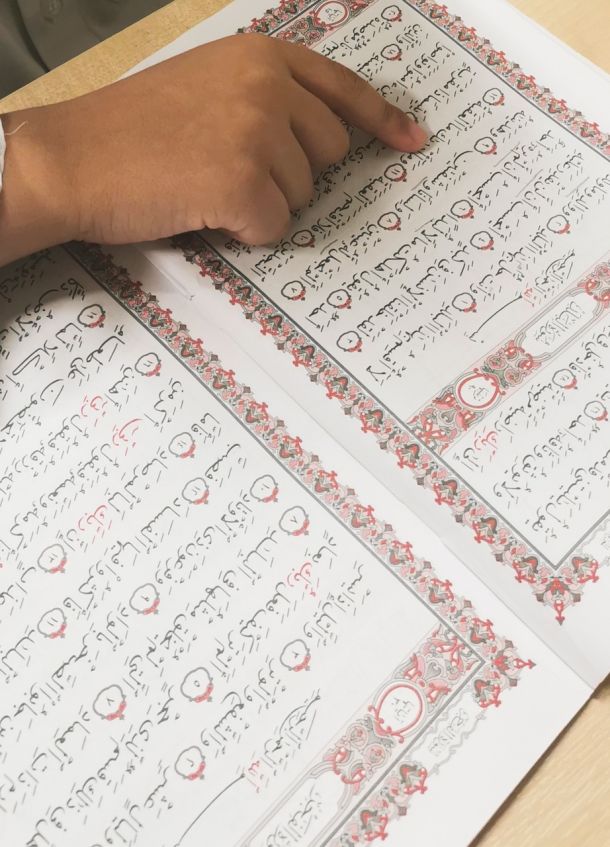 A child’s hand following the text of a Qur’an during a Karima weekday lesson