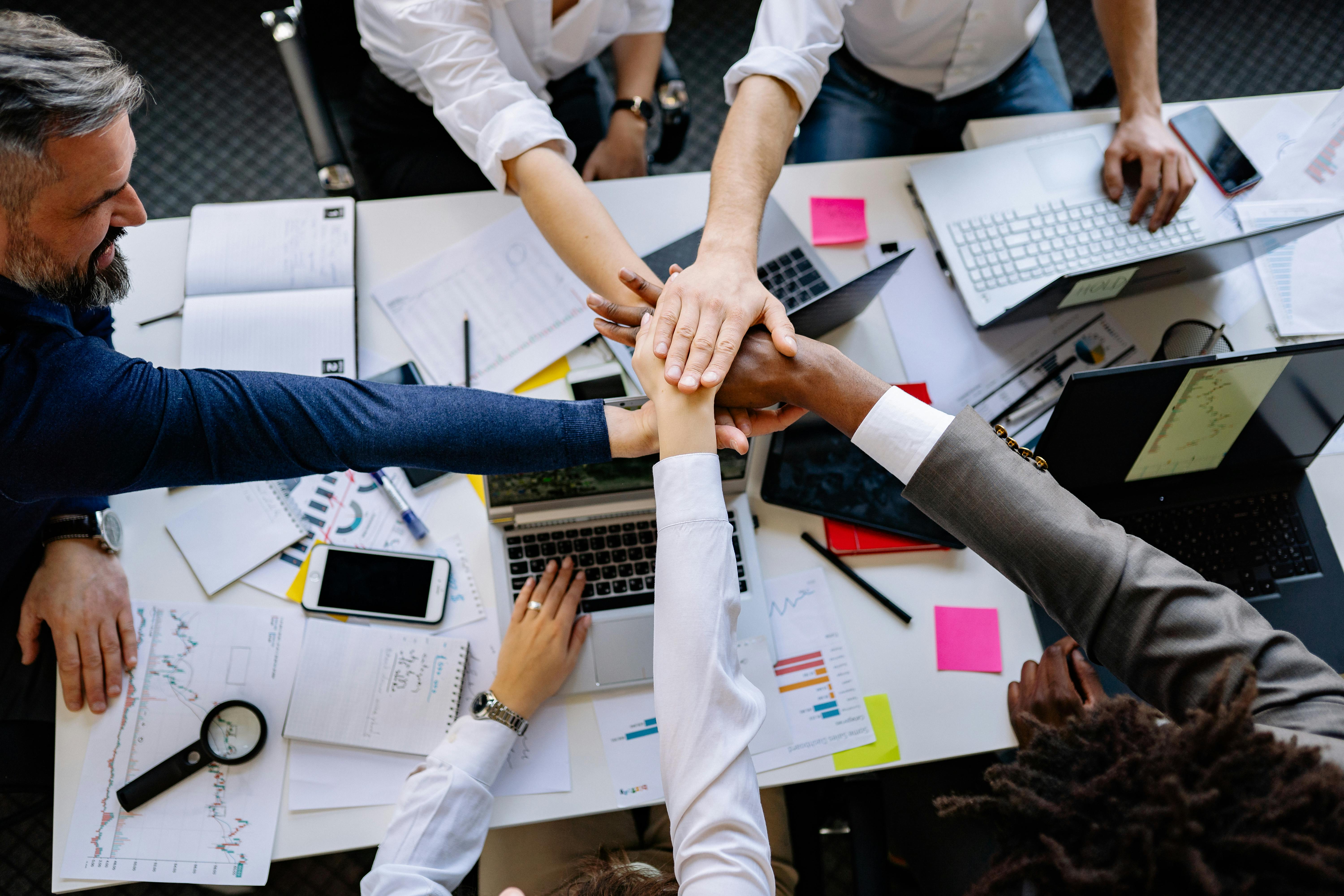 high-angle-shot-of-diverse-hands-together-over-a-desk-with-laptops-and-paperwork - yan-krukau (pexels)